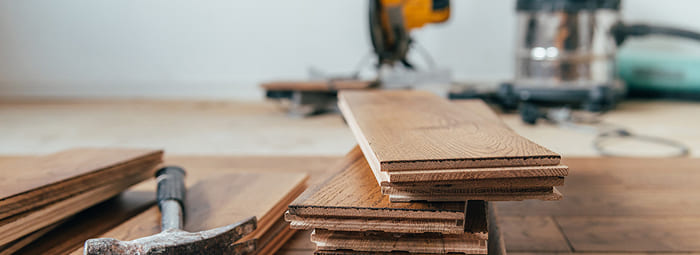 Stack of hardwood flooring planks with installation tools in the background.